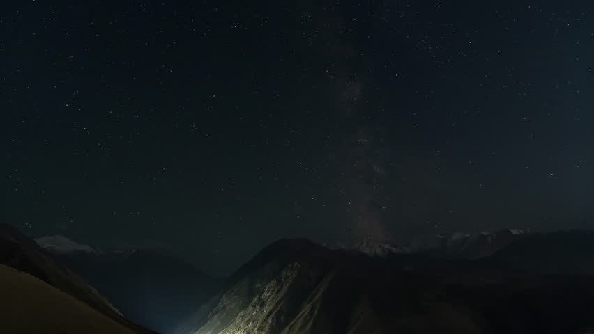 Night sky over mountainous landscape time lapse. Tian Shan mountain range. Stars and Milky Way visible in clear sky.