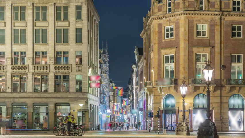 The Dam square in Amsterdam night timelapse, The Netherlands. The place is the historical center of the city and includes museum, shops and hotels. Illuminated Kalverstraat street