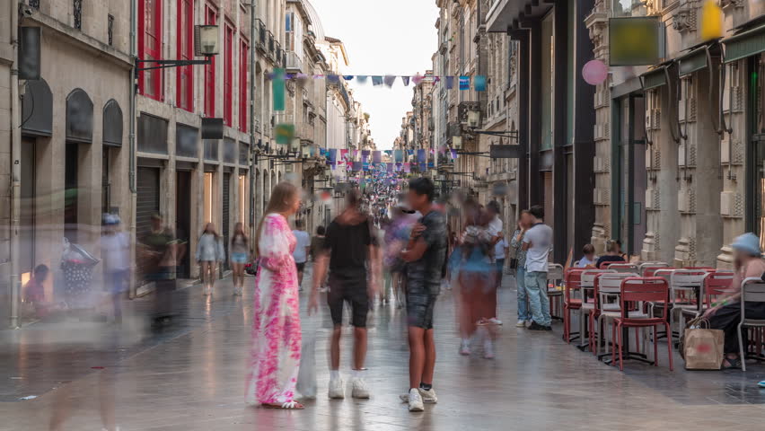 Tourists and locals walking and shopping in Rue Sainte-Catherine timelapse, Bordeaux, France. The longest pedestrian street in the country. Colorful flags decorate the street. Atmosphere of urban life