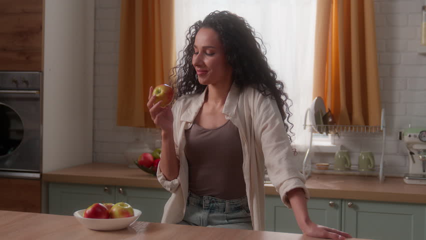 Hispanic woman Latina girl female lady Caucasian homeowner diet nutrition good habit throwing apple in air eating bite fruit smiling healthy food health care at home kitchen vitamin minerals eat happy