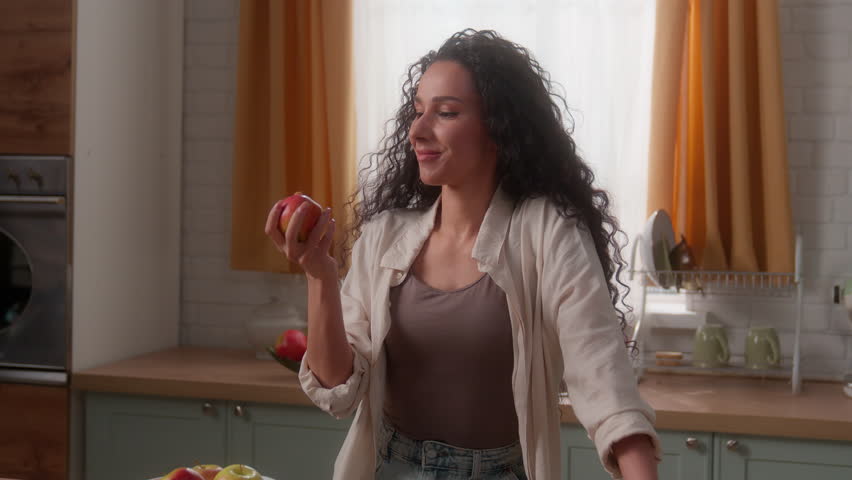 Hispanic woman Latina girl female lady Caucasian homeowner diet nutrition good habit throwing apple in air eating bite fruit smiling healthy food health care at home kitchen vitamin minerals eat happy