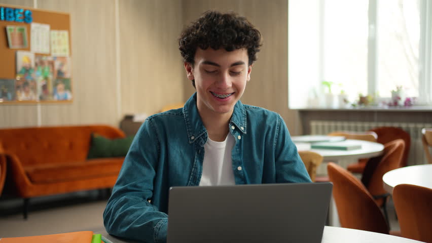 Smiling Caucasian man male teenage happy guy student schoolboy pupil modern technology service study exam using laptop computer e-learning learn studying online internet education in school university