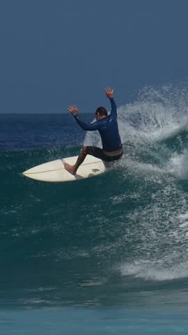 Male surfer ridding a wave under blue sky in a hot sunny day. Vertical slow motion video. Maldives