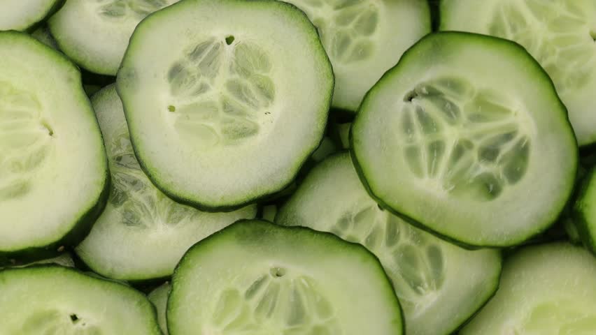 Rotating slides of fresh cucumber in close-up. Green cucumber slices moving in a circular motion. Healthy vegetable background with fresh cucumber slices. top view