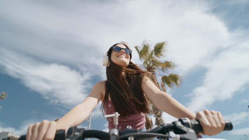 Video of pretty young woman listening music with headphone while enjoying with bike strolling along the seafront