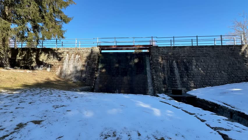 A winter scene shows a stone bridge over a snowy landscape under a clear blue sky, inviting adventure