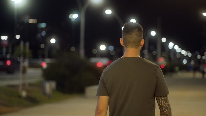 Focused man walking under city lights at night, maintaining a determined expression. Slow rotation camera movement captures the atmosphere and emotion of the scene.