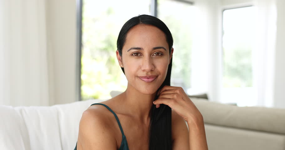 Positive beautiful young New Zealander girl looking at camera, getting happy, cheerful, laughing, touching facial skin, opening perfect white teeth. Home head shot portrait of young Maori woman