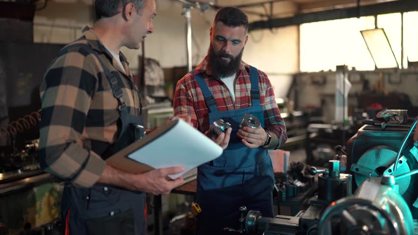 Skilled metal industry workers collaborating while inspecting precision manufactured part, discussing production details inside industrial workshop