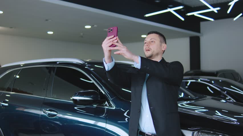 Businessman taking a selfie with a new SUV in a car showroom while smiling and enjoying the moment during a busy afternoon visit to the dealership