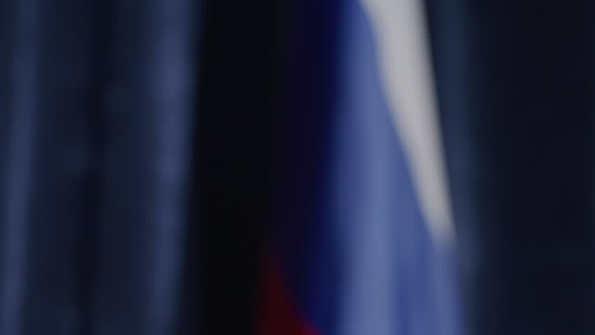 Close-up view of two male diplomats in formal suits shaking hands in front of Russian flag during political press conference
