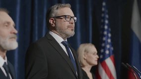 Middle-aged political leader standing with team on stage with American and Russian flags in background, making public announcement during press conference. Tilt-up shot - Powered by Shutterstock - Get 15% off with code: PIKWIZARD15