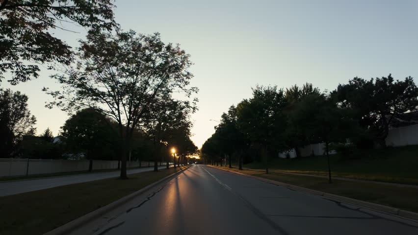 The wide shot from the moving car along the road in suburb area in the USA neighborhood on a beautiful sunny morning or evening. 