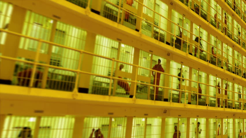 Camera moves past rows of prisoners serving time in a large cell block.