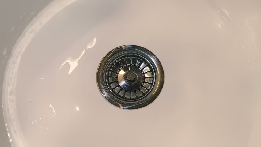 A man's hand opens the drain plug in a white round sink and water swirls into the drain. Closeup. Macro. Slow mo, slow motion, high speed camera, 250fps