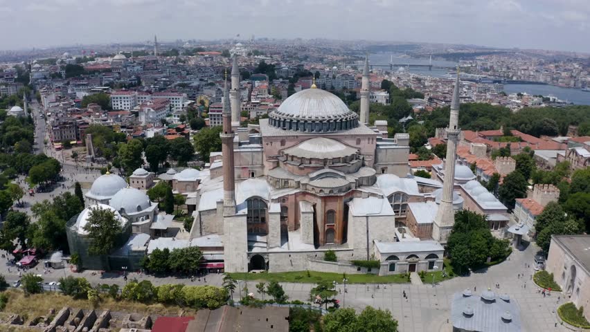 Aerial perspective showcasing Hagia Sophia with its grand dome and minarets against vibrant skyline of Istanbul. Lush greenery surrounds historical site, capturing essence of city.