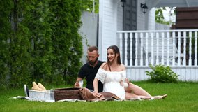 Caucasian couple sit on the plaid on the green grass outdoors. Man and woman drink milk at the picnic. - Powered by Shutterstock - Get 15% off with code: PIKWIZARD15