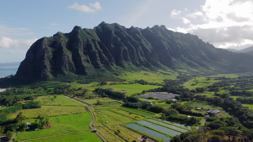 Kualoa Ranch Hawaii - majestic green mountains tower over lush valley with farms and ponds, capturing iconic tropical landscape and cinematic natural beauty