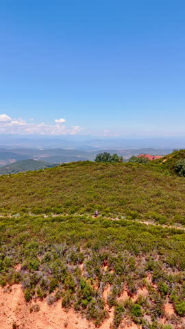 Trail in the grass on the mountain top. Tourists stand on the path. Drone footage revealing view on the rocky landscape at backdrop. Vertical video.