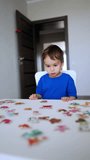 Smart cute toddler kid looks at the puzzles scattered on the desk in front of him. Kid picks the pieces playing a game. Vertical video. - Powered by Shutterstock - Get 15% off with code: PIKWIZARD15