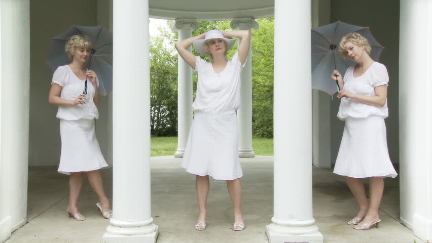Three identical girls standing in a gazebo. The two at the sides hold blue silk parasols and watch the one in the middle who is posing or moving to unheard music.