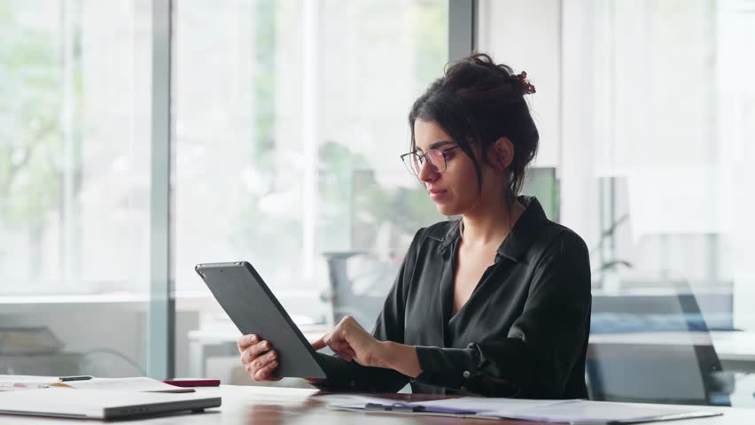 Smiling latina young professional business woman looking at pc device computer screen. Indian female businesswoman specialist holding digital tablet, using tab pad financial app at work in office - Powered by Shutterstock - Get 15% off with code: PIKWIZARD15