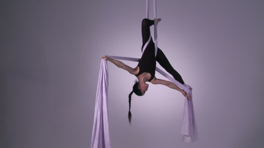 Athletic young woman supports herself in two inverted poses while doing aerial