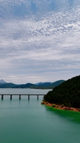 Long bridge above the lake in the national park of Leon, Spain, Europe. Aerial perspective on the beautiful mountainous landscape and turquoise waterscape. Vertical video.