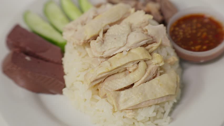 Traditional Hainanese chicken rice dish consisting of tender sliced chicken meat, chicken offal, and cucumber slices place on rice Served with a small bowl of flavorful dipping sauce