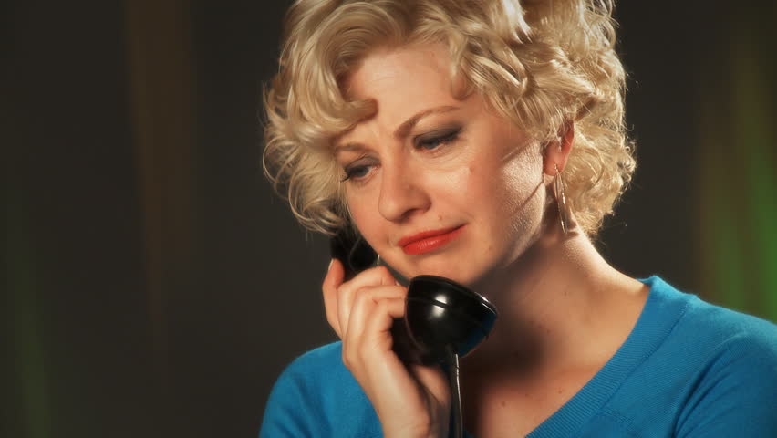Blonde girl in a turquoise dress listens to a caller on a retro phone. Close up.