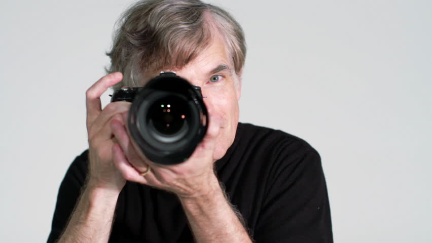 Man takes photographs with zoom lens in studio. Close up, facing camera.