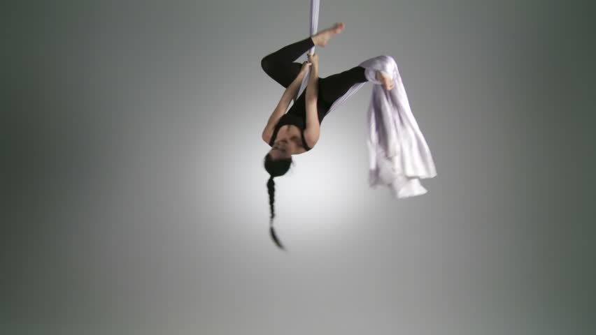 Athletic young woman suspends herself upside down while doing aerial yoga. Wide
