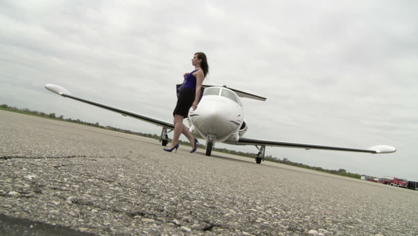 Girl walks across a runway infront of a private jet. Long shot from front with