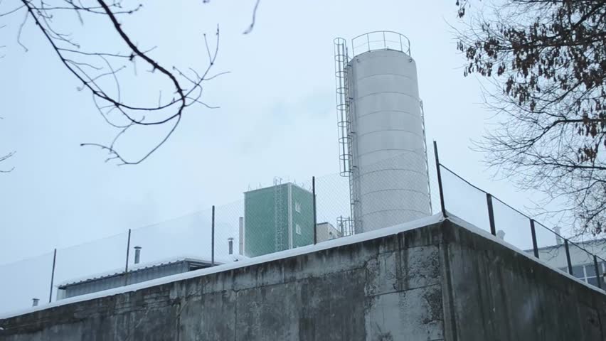 Large white tank is on top of a concrete wall. The sky is overcast and the weather is cold