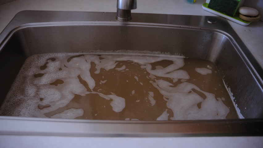 Stainless steel sink filled with murky, brown water, a drainage issue, clogged pipes, or contaminated water supply. Dirty water is coming back to the sink.