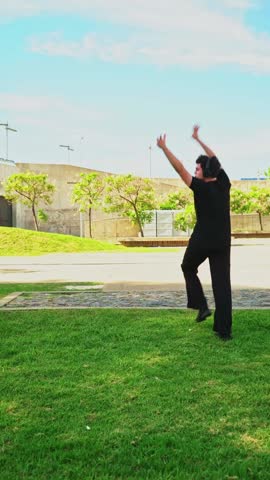 Young man dressed in black dancing festively while listening to music on his headphones in a park
