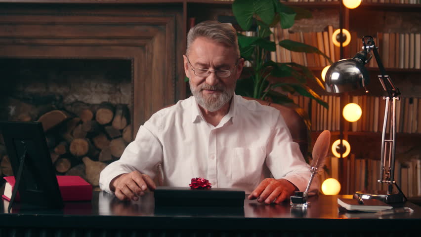 Excited elder Caucasian man holding box bow open surprise gift celebrating birthday male surprised happy old senior indoors grandfather holiday businessman pensioner business office congratulate home