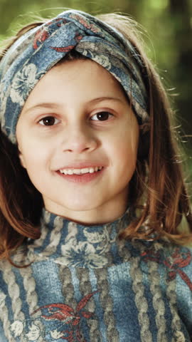 Vertical Format Video of Portrait of confident stylish young little kid girl standing in autumn park looking at camera and crossing arms fashion style. Young beautiful smiling girl crossed her arms.