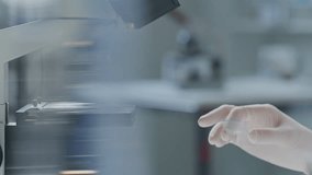 Gloved hands of unrecognizable scientist adjusting specimen slide on microscope stage for research in laboratory. Close-up, shallow focus shot - Powered by Shutterstock - Get 15% off with code: PIKWIZARD15