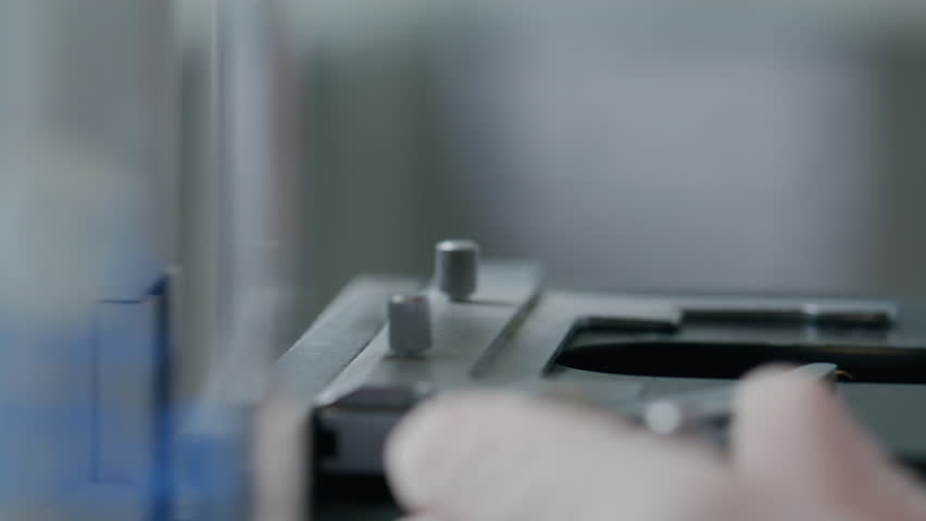 Hand of unrecognizable scientist positioning glass slide with leaf sample on illuminated microscope stage for laboratory analysis. Extreme close-up view
