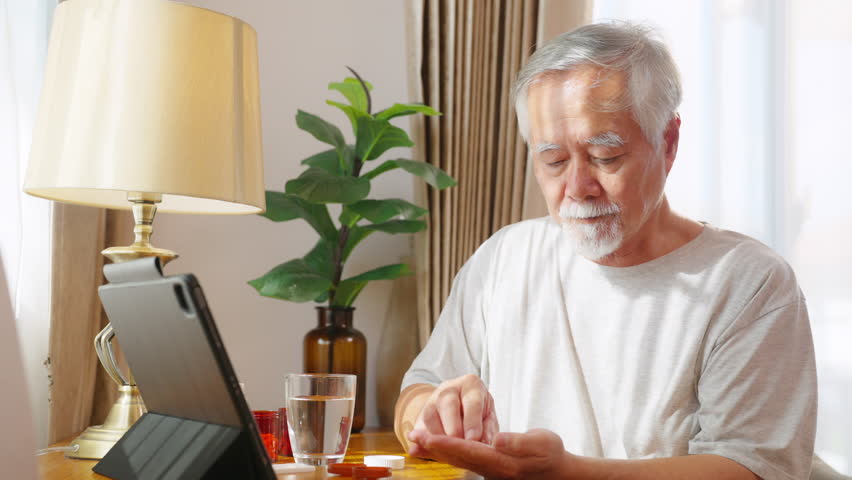 Asian senior man patient taking medicine pill with drinking water from a glass for relief disease in bedroom. Healthy elderly retired people taking vitamins complex supplement for self-care at home.