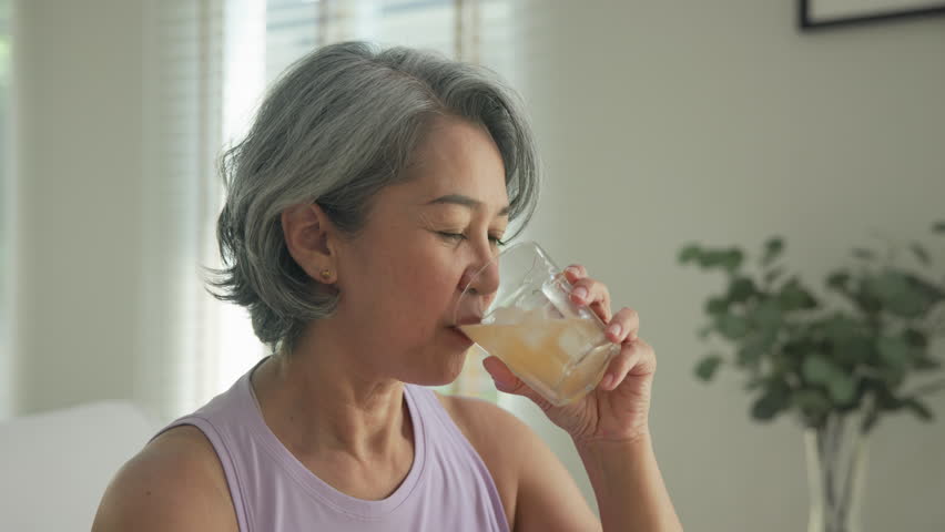 Asia adult people middle age happy old woman pour weight loss tea fiber juice drink kombucha gut health care diet detox sit at home sofa elder aging asian aged female. Fresh bottle medical food relief