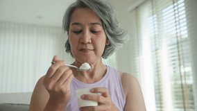 Asia adult people middle age happy old woman eat greek yogurt cup weight loss protein gut health care diet detox sit at home sofa elder aging asian aged female. Fresh medical food relief meal enjoy. - Powered by Shutterstock - Get 15% off with code: PIKWIZARD15