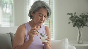 Asia adult people middle age happy old woman eat greek yogurt cup weight loss protein gut health care diet detox sit at home sofa elder aging asian aged female. Fresh medical food relief meal enjoy. - Powered by Shutterstock - Get 15% off with code: PIKWIZARD15