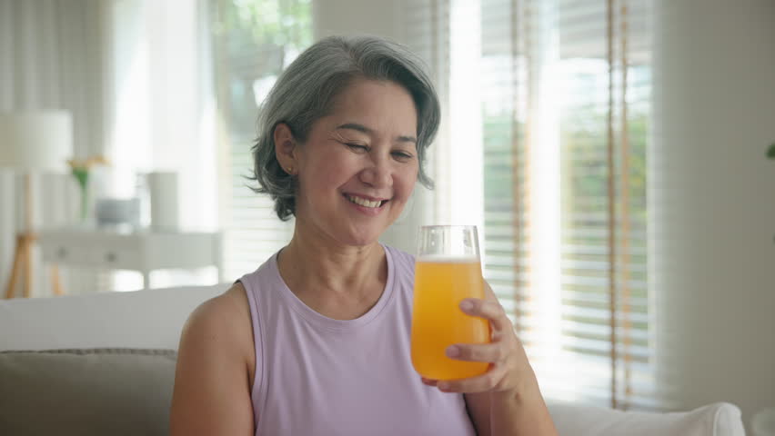 Asia adult people middle age happy old woman smile drink vitamin d c e k zinc water pill reduce hot flash dry skin health care sit at home sofa elder aging asian aged female. Take diet food relief