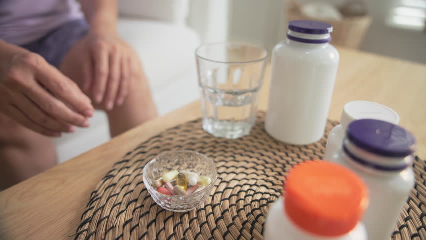 Asia adult aged people middle age happy old woman smile drink vitamin d c e k zinc omega 3 fish oil water pill reduce hot flash dry skin health care sit at home sofa elder aging asian. Take diet food.