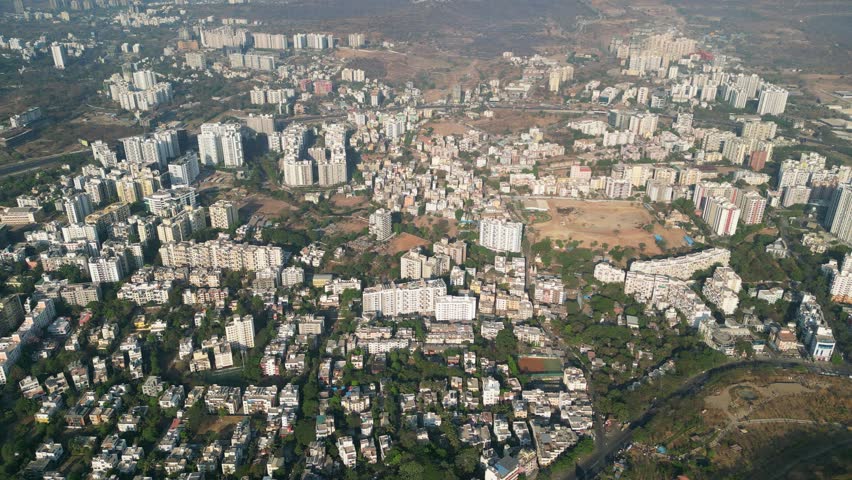 An aerial video shows a service road, fast-moving automobiles, and residential and commercial buildings on an Indian highway expanding quickly. The Metro train bridge is currently being built,