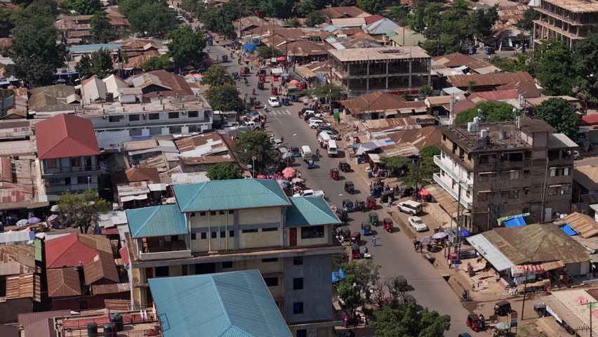 An aerial perspective of Moshi, Tanzania, highlighting the dynamic market scene and traffic. People walk along the busy streets, while vehicles and motorbikes move through the city center