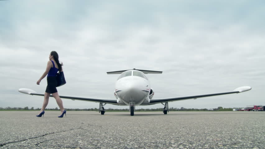 Girl walks across a runway infront of a private jet. Long shot from front,