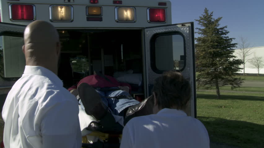 Two paramedics load an unconscious patient on a stretcher into an ambulance.